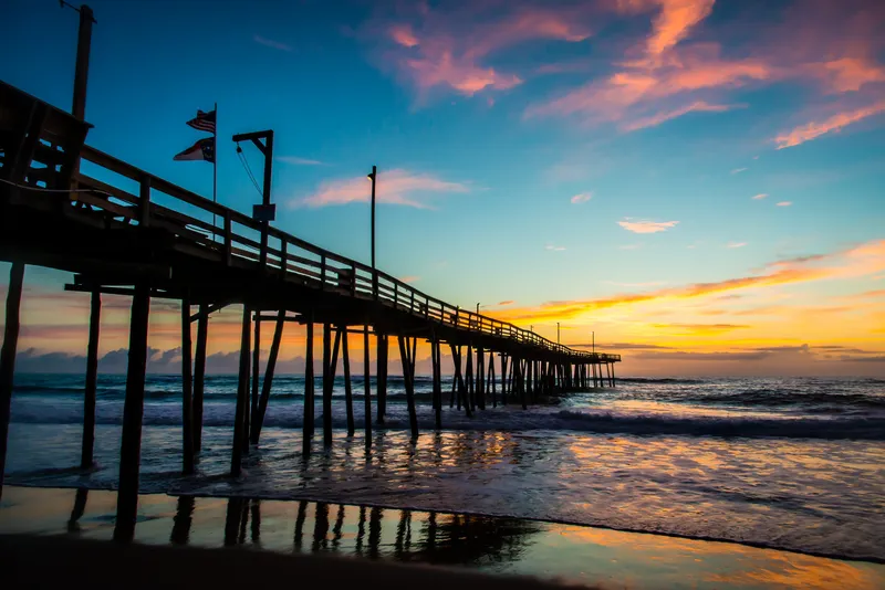 Outer Banks fishing pier at sunrise with warm light reflecting off calm ocean water