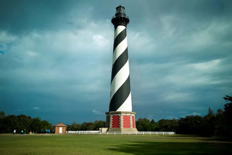 Cape Hatteras Lighthouse with its iconic black and white diagonal stripes against a blue sky, viewed from the surrounding grounds at Buxton