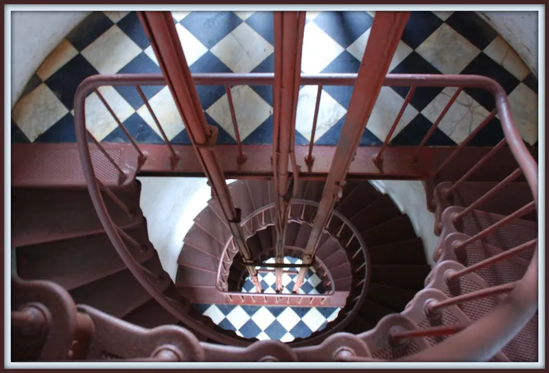 Looking up through the spiral staircase inside the Cape Hatteras Lighthouse, iron steps curving upward toward the light