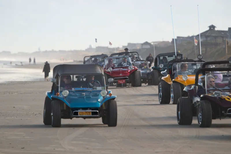 Dune buggies driving on the beach at the Outer Banks, with tire tracks in the sand and ocean in the background