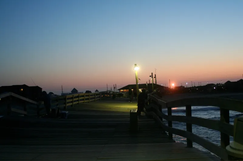 Golden sunset behind the Avon Pier with silhouetted pier structure extending over the ocean, warm orange and purple sky
