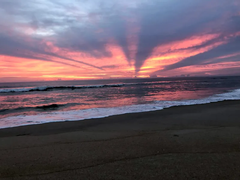 Early morning sunrise over Kill Devil Hills beach with warm orange light and calm ocean
