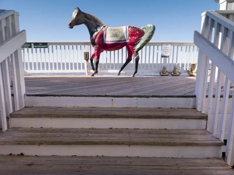 Daytime view of the wooden boardwalk at Duck Town Park with steps and horse statue, overlooking Currituck Sound on a clear fall day