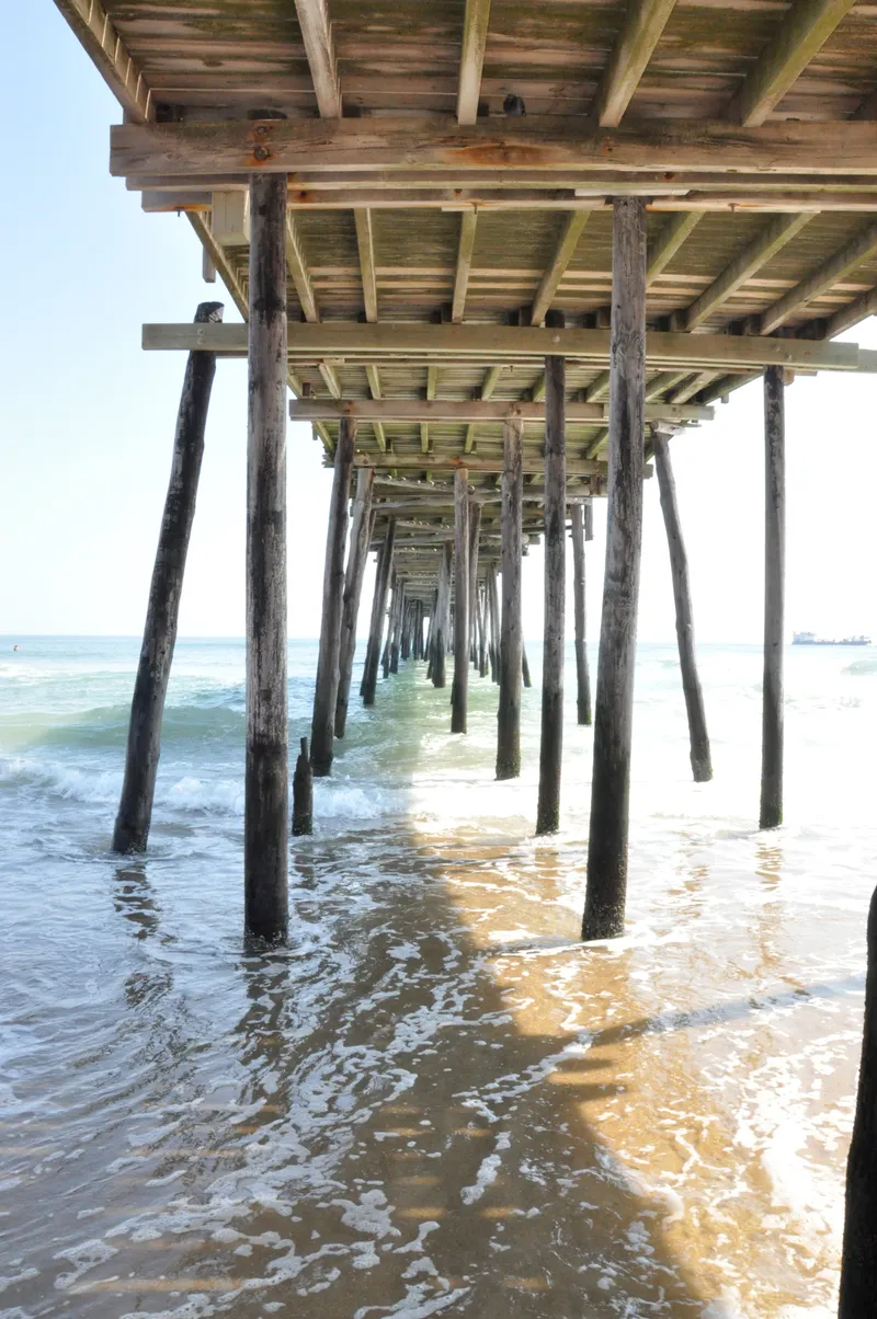Nags Head Pier from the beach with ocean waves and cloudy sky