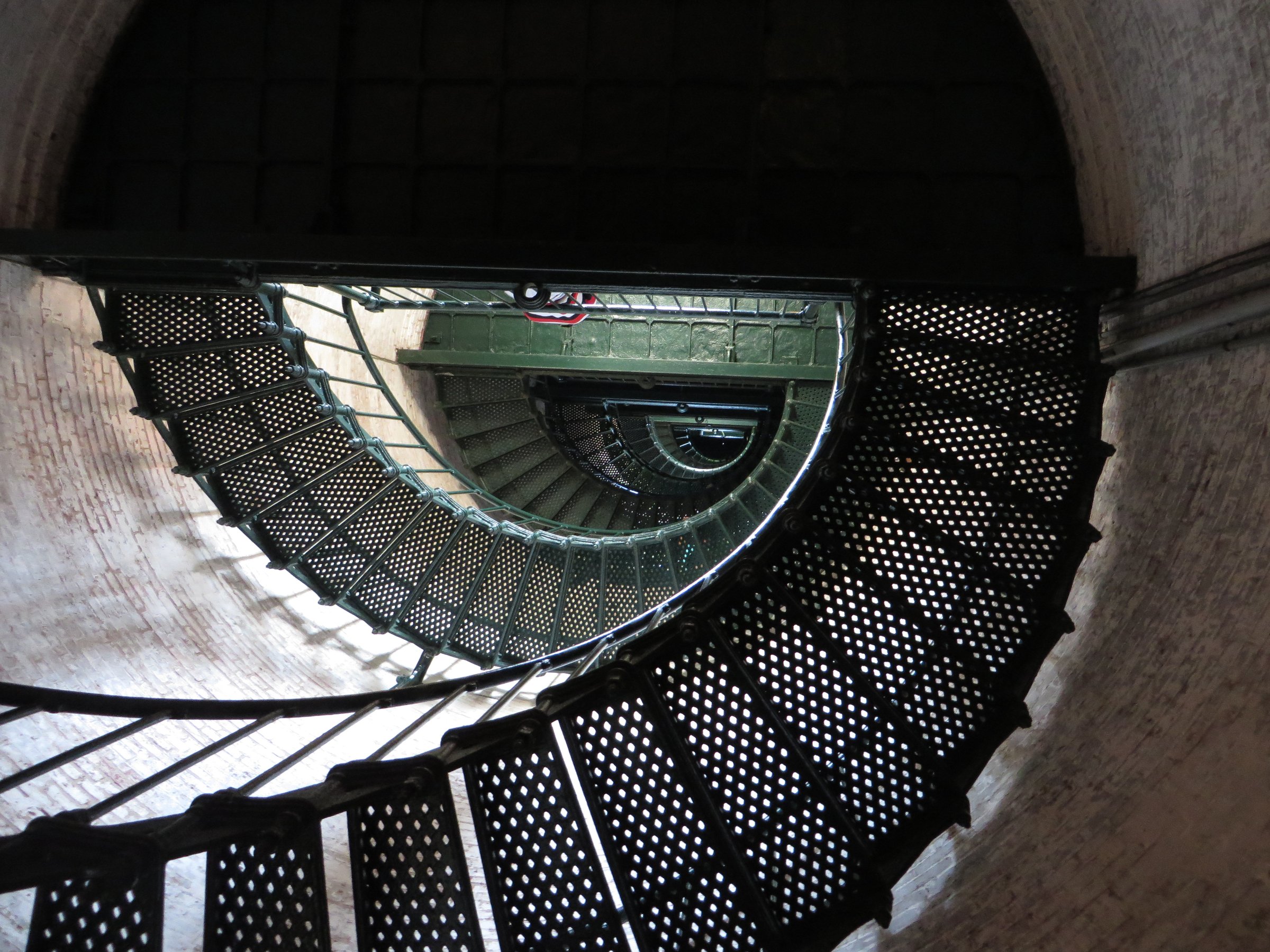 Currituck Beach Lighthouse rising above the tree line in Corolla, its unpainted red brick exterior visible against a blue sky
